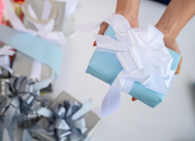 Primo piano delle mani femminili che incartano i regali per il nuovo anno La donna tiene il regalo di Natale fatto a mano Preparazione per la vacanza Scatola con un inchino Desktop con carta da imballaggio