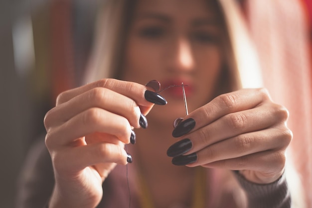 Primo piano delle mani femminili che passano il filo attraverso l'ago. Concetto d'epoca.