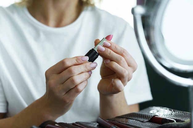 Primo piano delle mani femminili che tengono il rossetto rosa del tubo