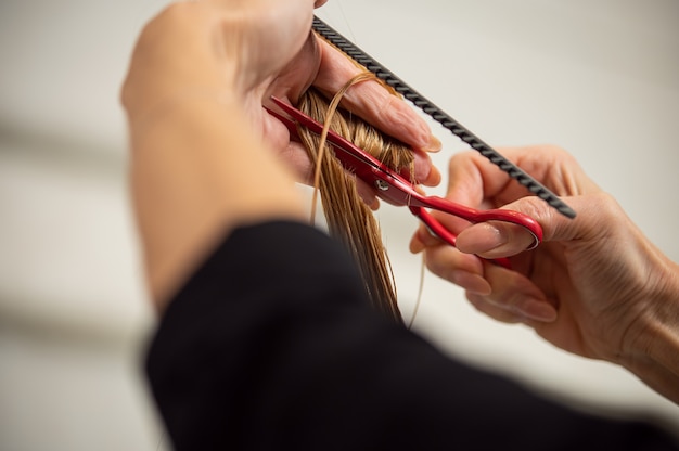 Primo piano delle mani femminili che tengono le forbici del parrucchiere e che tagliano i capelli biondi lunghi