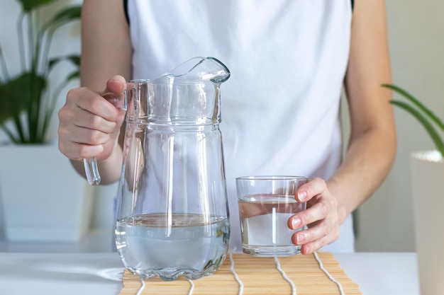 Primo piano delle mani femminili che versano acqua potabile in un bicchiere rituali mattutini per la salute