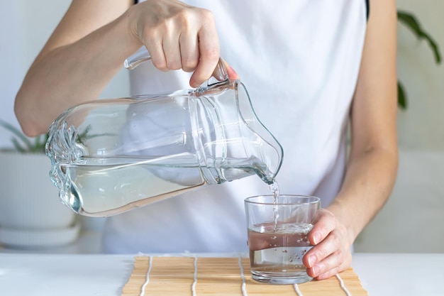 Primo piano delle mani femminili che versano acqua potabile in un bicchiere rituali mattutini per la salute