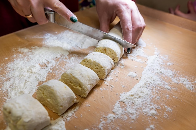 Primo piano delle mani femminili nella farina con una salsiccia di pasta tagliata a coltello in piccoli pezzi