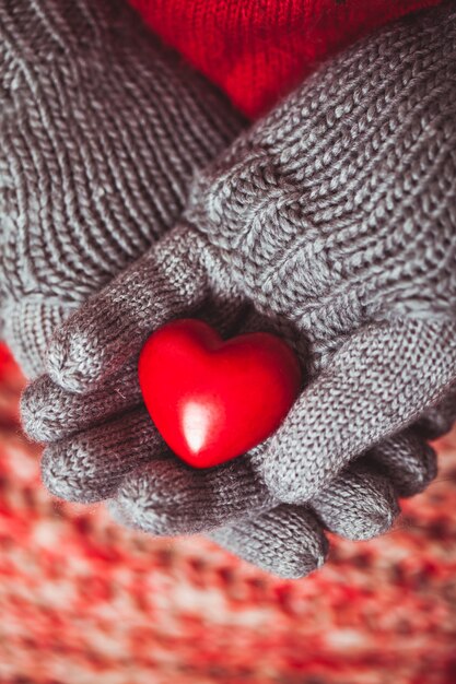 Primo piano delle mani in guanti lavorati a maglia grigi che tengono cuore rosso