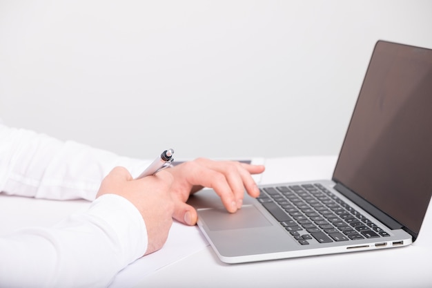 Primo piano delle mani maschili che digitano sulla tastiera del laptop mentre si lavora alla scrivania bianca.