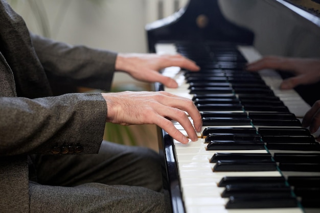 Primo piano delle mani maschili che spingono sui tasti del pianoforte a coda e suonano la musica classica a lezione