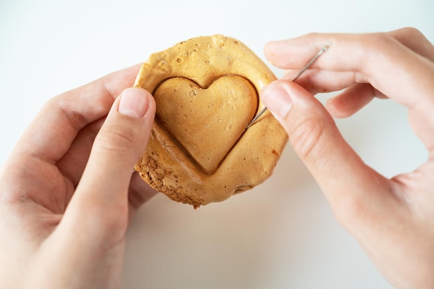 Primo piano delle mani scratch zucchero di canna caramello caramelle biscotti con un ago di metallo a forma di cuore ...