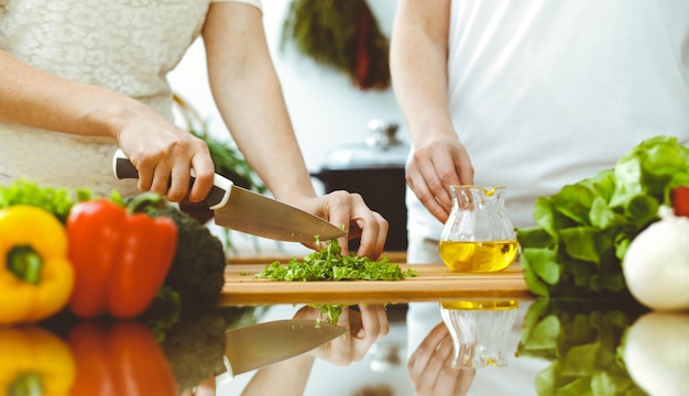 Primo piano delle mani umane che cucinano in cucina. Madre e figlia o due amiche che tagliano le verdure per insalata fresca. Amicizia, cena in famiglia e concetti di stile di vita.