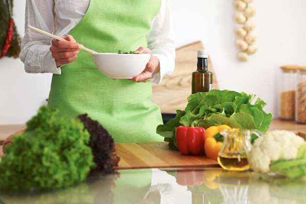 Primo piano delle mani umane che cucinano insalata di verdure in cucina sul tavolo di vetro con la riflessione. Pasto sano e concetto vegetariano