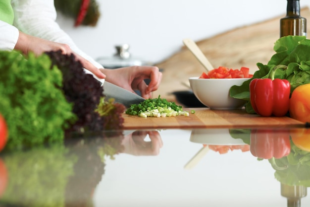 Primo piano delle mani umane che cucinano insalata di verdure in cucina sul tavolo di vetro con la riflessione. Pasto sano e concetto vegetariano