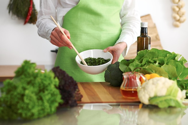 Primo piano delle mani umane che cucinano insalata di verdure in cucina sul tavolo di vetro con la riflessione. Pasto sano e concetto vegetariano