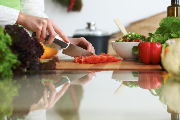 Primo piano delle mani umane che cucinano insalata di verdure in cucina sul tavolo di vetro con la riflessione. Pasto sano e concetto vegetariano