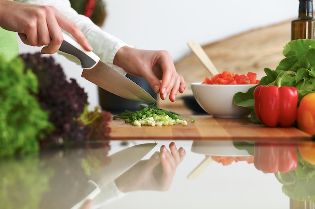 Primo piano delle mani umane che cucinano insalata di verdure in cucina sul tavolo di vetro con la riflessione. Pasto sano e concetto vegetariano