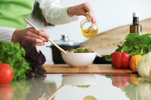 Primo piano delle mani umane che cucinano insalata di verdure in cucina sul tavolo di vetro con la riflessione