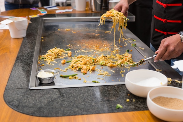 Primo piano dello chef che prepara porzioni singole di spaghetti saltati in padella su Flat Top Grill