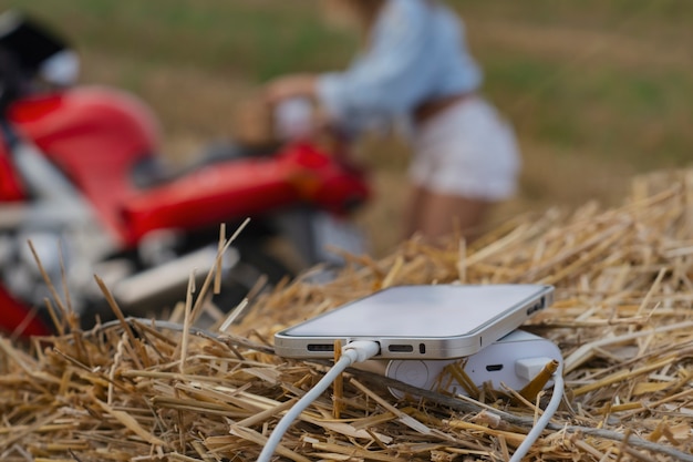 Primo piano dello smartphone con un caricatore portatile. Power Bank carica il telefono sullo sfondo di una moto, una ragazza e la natura.