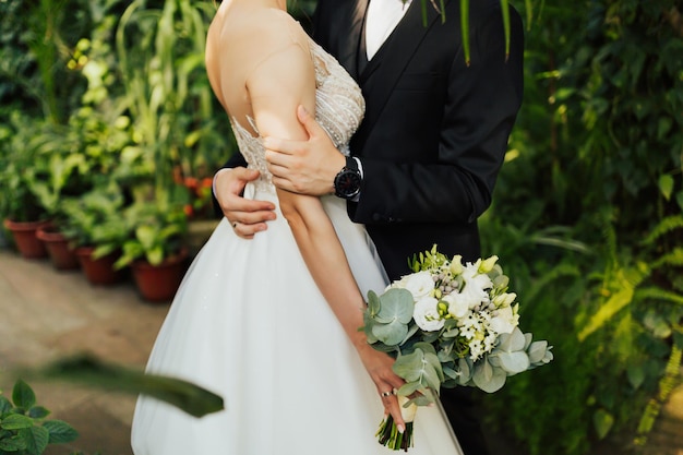 Primo piano dello sposo che abbraccia sua moglie e lei che tiene il bellissimo bouquet da sposa classico con flusso bianco