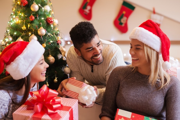 Primo piano di amici felici che tengono i regali mentre era seduto in camera da letto. . Concetto di vacanze di Natale.