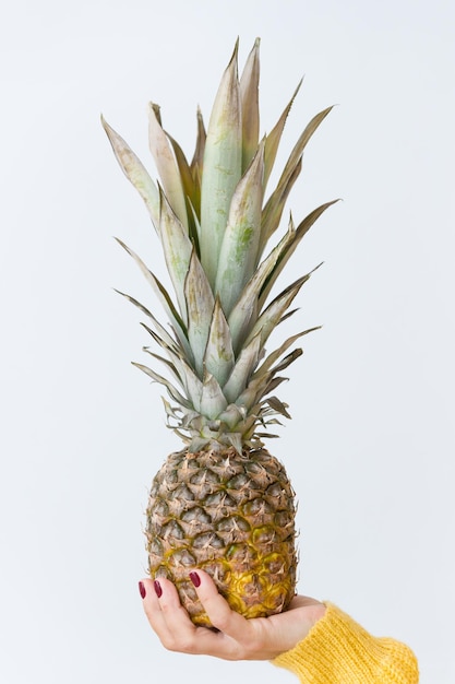 Primo piano di ananas fresco e succoso in mano a una donna nel mezzo di uno sfondo azzurro.