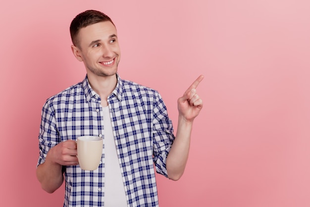 Primo piano di bel giovane uomo felice sorriso positivo bere caffè punto dito spazio vuoto isolato sfondo pastello