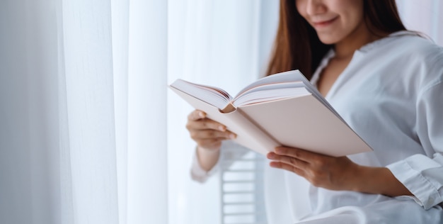 Primo piano di bello libro di lettura asiatico della donna in una camera da letto a casa