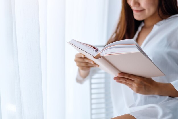 Primo piano di bello libro di lettura asiatico della donna in una camera da letto a casa