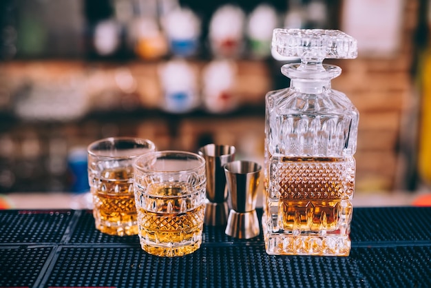 Primo piano di bicchieri di cristallo per bottiglie di whisky e strumenti per cocktail nel moderno bar sul bancone