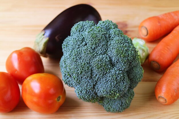 Primo piano di broccoli crudi con pomodori carote e melanzane su sfondo di legno