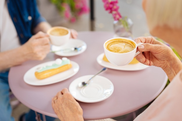 Primo piano di caffè in attesa da mani femminili mentre eclairs in attesa sulla superficie