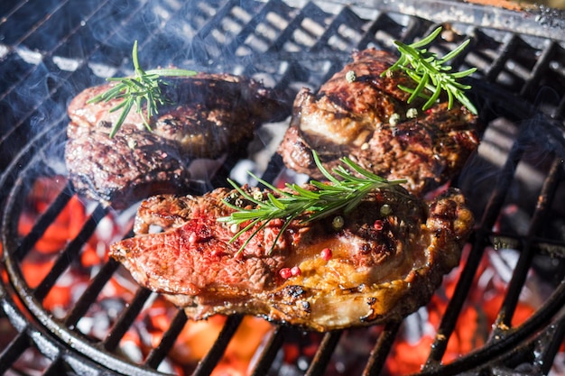 Primo piano di carne alla griglia con rosmarino fresco in cima Utilizzo di erbe aromatiche per rendere speciale il gusto di carne alla griglia Primo piano di carne cotta alla fiamma del barbecue sullo sfondo