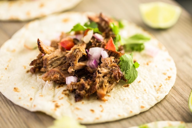 Primo piano di carnitas di maiale tirato con pico de gallo su una tortilla di farina.