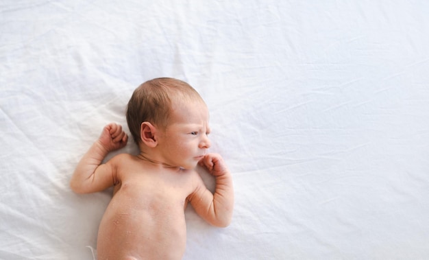 Primo piano di caucasico peloso brunet carino neonato sdraiato sulla schiena su foglio biancoNaked una settimana bambino mezzo corpo colpo copia spazio per testoAlto angolo vista dall'alto