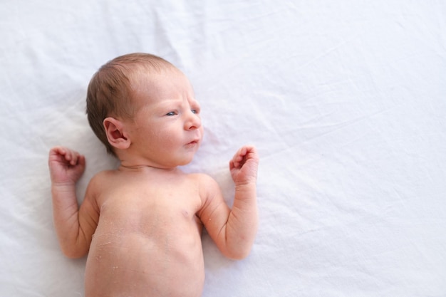 Primo piano di caucasico peloso brunet carino neonato sdraiato sulla schiena su foglio biancoNaked una settimana bambino mezzo corpo colpo copia spazio per testoAlto angolo vista dall'alto