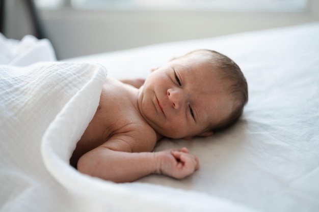 Primo piano di caucasico peloso brunet carino neonato yawningFew pochi giorni bambino sul letto sotto coperta bianca