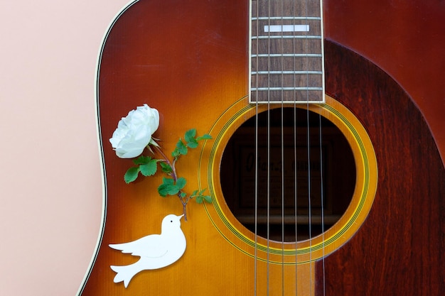 Primo piano di chitarra acustica e una colomba della pace con una rosa bianca nel becco su sfondo pastello Vista dall'alto primo piano spazio di copia