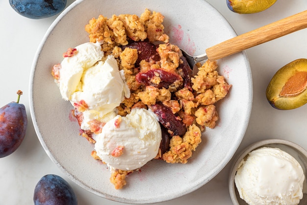 Primo piano di crumble di prugne con gelato alla vaniglia in un piatto. Dolce estivo di frutta croccante. Vista dall'alto