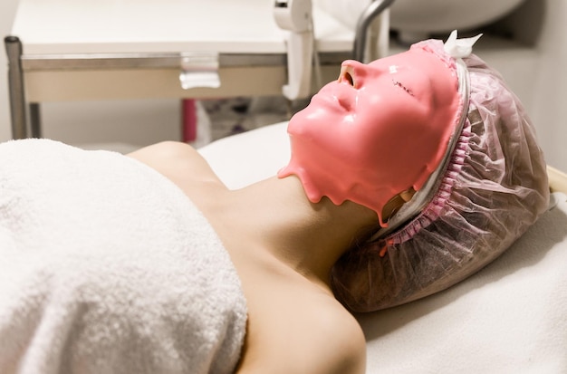 Primo piano di cura della pelle della donna di bella ragazza con la maschera cosmetica sulla pelle del viso nel salone di bellezza Giovane donna con il viso coperto di trattamento di bellezza della maschera di alginato idratante rosa