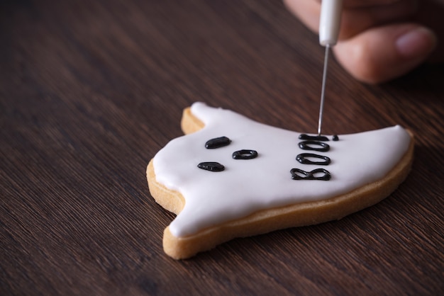 Primo piano di decorare biscotti di panpepato fantasma carino Halloween con glassa glassa crema topping bag.