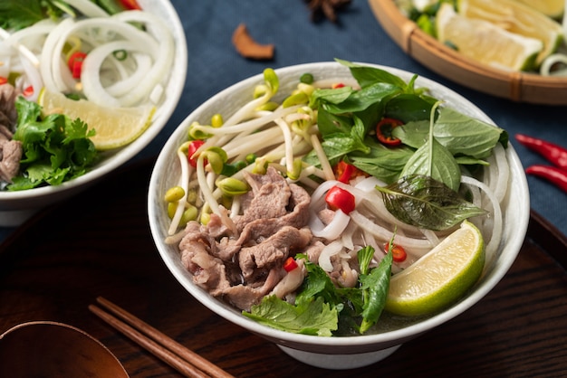 Primo piano di deliziose tagliatelle di manzo vietnamite pho in una ciotola con ingredienti con spazio di copia.