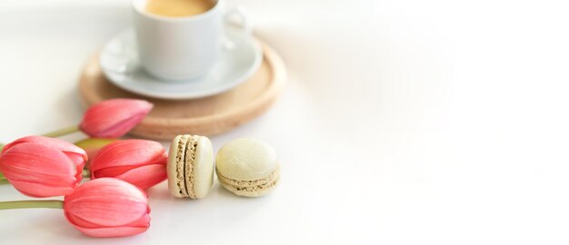 Primo piano di dolci macarons francesi tazza di tè o caffè e fiori primaverili su sfondo bianco Spazio per il testo