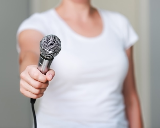 Primo piano di donna in camicia bianca, che offre a qualcuno di darle un'intervista. Tenendo il microfono in mano.
