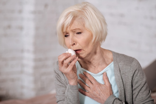 Primo piano di donna piuttosto invecchiata tenendo il tovagliolo e tosse molto forte.