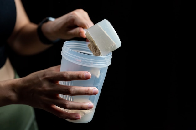 Primo piano di donne con misurino di proteine del siero di latte e bottiglia shaker, preparazione frullato di proteine.