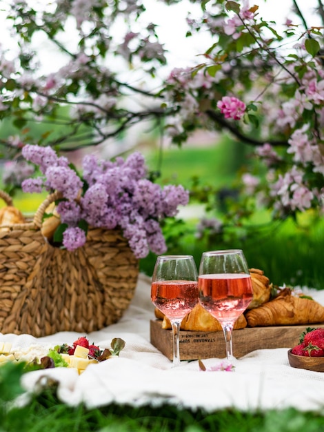 Primo piano di due bicchieri di vino rosato cestino da picnic croissant cibo e fiori sul banner di erba