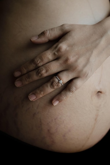 Primo piano di due mani che indossano fedi nuziali su una donna incinta che tocca la sua grande pancia