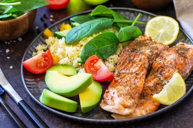 Primo piano di filetto di salmone alla griglia con insalata di cous cous verdure fresche e avocado su sfondo scuro