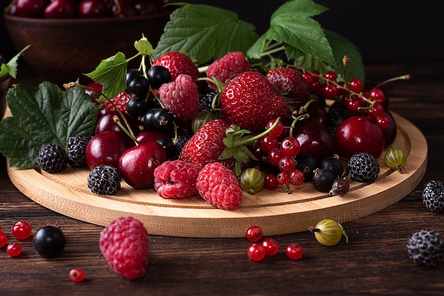 Primo piano di fragole, lamponi, ciliegie, ribes, uva spina su uno sfondo di legno scuro, cibo sano estivo.