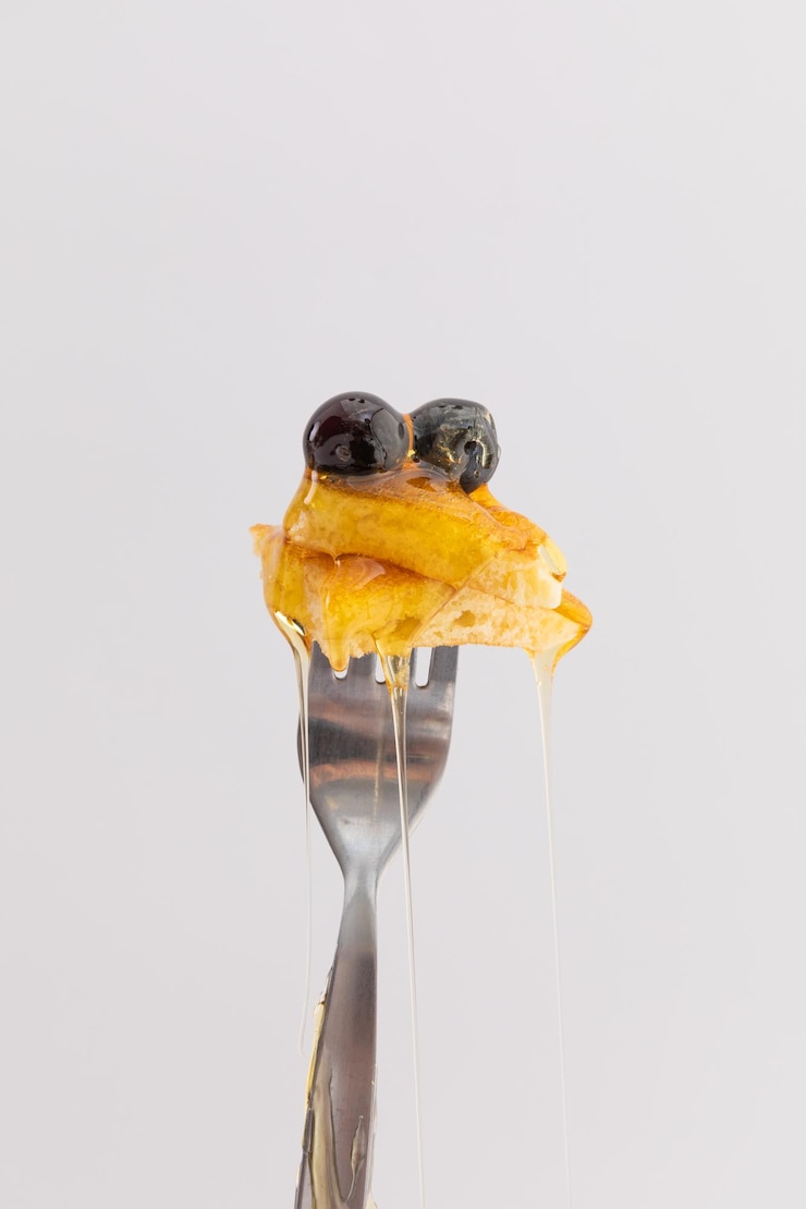 Foto primo piano di frittella e frutti di bosco con miele gocciolante sulla forcella su sfondo bianco. concetto di spazio copia divertente dessert alimentare.
