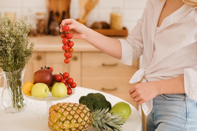 Primo piano di frutta verdura sul tavolo della cucina che cucina La padrona di casa tiene in mano piccoli pomodori