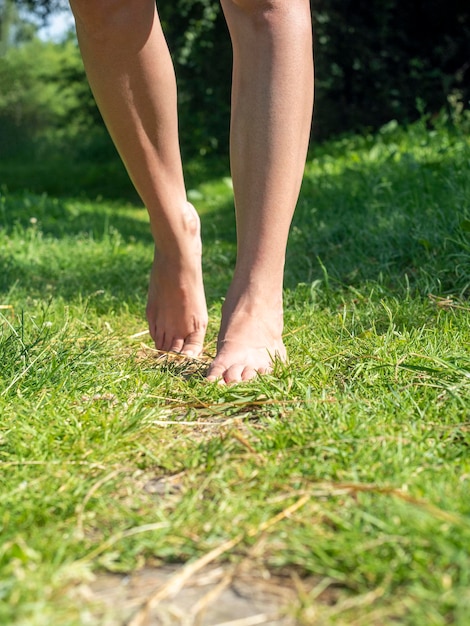 Primo piano di gambe femminili eleganti che camminano a piedi nudi sull'erba verde in estate